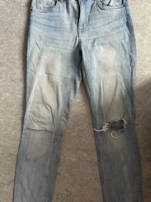 Ljusblå slitna skinny jeans - Säljer ett par ljusblå skinny jeans med slitning och hål på ena knät. Jeansen har klassisk femficksmodell och hög midja. Perfekta för en avslappnad och trendig look. Materialet är denim i bomull.