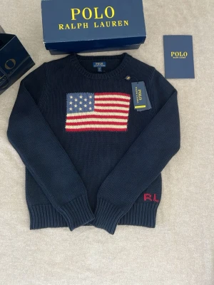 Polo Ralph Lauren - Säljer en stilig kabel stickad polo Ralph Lauren med en usa flagga på.Tröjan är Perfeckt för sommaren.Och tröjan är liten i storleken skulle rekommendera ålder 12-14/15 158-170 cm max.Tillbehör ingår tyvärr inte i priset bara tröjan ingår.👍🏻