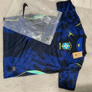 Brazil away shirt - Snygg blå fotbollströja från Nike med Brasilien CBF-logga och gula detaljer. Tröjan har korta ärmar, rund hals och ett mönster i olika blå nyanser. Perfekt för träning eller match och har officiella märken tryckta på bröstet.