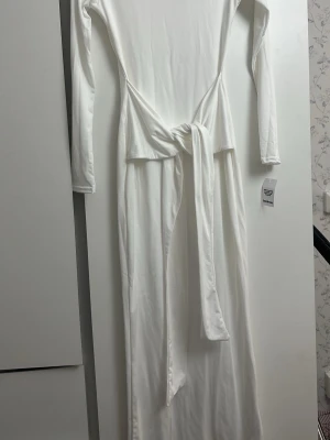 Vit långärmad maxiklänning med knyt - Säljer en stilren vit långklänning med långa ärmar och ett snyggt knyt i midjan. Klänningen har en rak passform och är tillverkad i ett mjukt, stretchigt material som ger en bekväm känsla. Perfekt för dig som gillar minimalistisk och elegant stil.