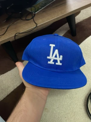 Blå LA Dodgers keps - Snygg blå keps från New Era med LA Dodgers-logga broderad i vitt framtill. Klassisk rak skärm och justerbar baksida. Perfekt för dig som vill ha en sportig och trendig look. Materialet är tåligt och kepsen har ventilerande hål upptill.