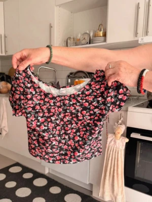 Blommig croppad topp med kort ärm - Söt croppad topp med svart botten och blommigt mönster i rosa och vitt. Toppen har korta ärmar och rund halsringning. Perfekt för dig som vill ha en trendig och somrig look.