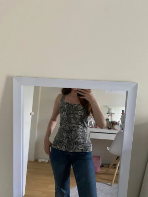 Ormmönstrad ärmlös topp - Säljer en snygg ärmlös topp med ormmönster i svart och beige. Toppen har en tight passform och breda axelband, perfekt för dig som vill sticka ut lite extra. Materialet känns mjukt och stretchigt, troligen polyester eller syntet. Storleken är S men passar XS