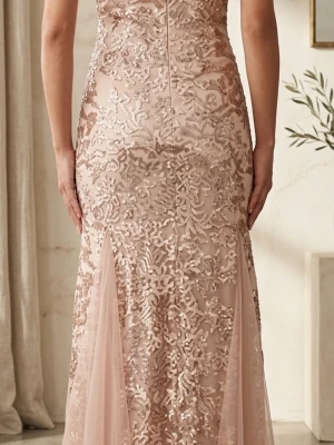 Lång champagnefärgad paljettklänning - Elegant långklänning i champagnefärg med glittriga paljetter och broderade detaljer. Klänningen har en figurnära passform och är ärmlös med vacker mesh och spetsapplikationer. Perfekt för dig som vill sticka ut med en lyxig look.