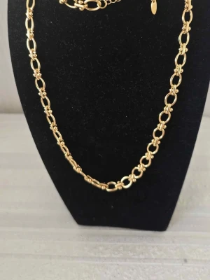 Guldfärgat kedjehalsband med ovala länkar rostfritt stål halsband med armband  - Snyggt halsband i guldfärg med ovala, sammankopplade länkar. Halsbandet har en justerbar kedja och stängs med ett klassiskt lås. Perfekt för att ge din outfit en trendig touch. Materialet är metall och designen är enkel men ändå iögonfallande.