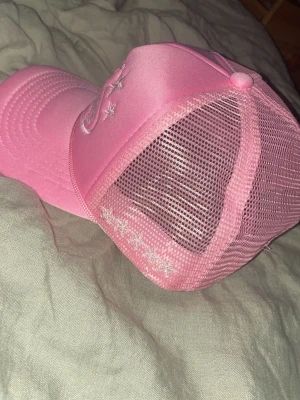 Helt ny Cortiez keps i perfekt skick - Snygg rosa truckerkeps med broderade stjärnor framtill och mesh på sidorna för extra ventilation. Kepsen har böjd skärm och justerbar baksida. Perfekt för dig som vill sticka ut med en färgglad accessoar.