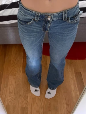 Blå bootcut jeans med låg midja - Säljer ett par klassiska blå bootcut jeans med låg midja och fem fickor. Jeansen har en snygg tvätt och är tillverkade i denim med lätt stretch. Perfekta för en avslappnad och trendig look.