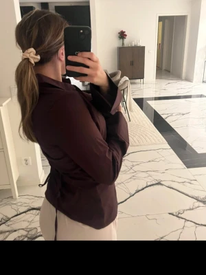 Shaped Tie Blouse Gina - Säljer en stilren mörkbrun skjorta med klassisk krage och knäppning framtill. Skjortan har långa ärmar och en rak passform som ger en clean look. Perfekt att styla till både jeans och kjol. Ny med prislapp!