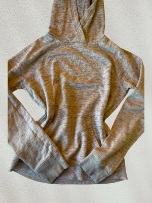 Gråmelerad hoodie från Hollister - Mysig gråmelerad hoodie från Hollister med broderad logga på bröstet. Hoodien har långa ärmar, ribbade muddar och en klassisk huva. Tillverkad i mjukt bomullsmaterial som känns skönt mot huden. Storlek S men finns några fläckar som syns på bilderna