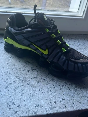 Nike Shox svarta och neon. - Nike Shox sneakers i svart med detaljer i neon-gult och silver. Skon har en futuristisk design med Shox-dämpning i sulan, mesh- och syntetmaterial samt tydlig S-logga bak. Perfekt för dig som gillar sportig och unik stil.