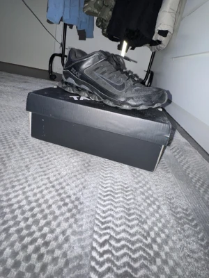 Nike Reax svarta sneakers - Svarta Nike Reax sneakers med mesh och syntetpaneler, robust sula och klassisk Swoosh på sidan. Skorna har snörning och sportig design som passar till streetwear och vardagsstil.
