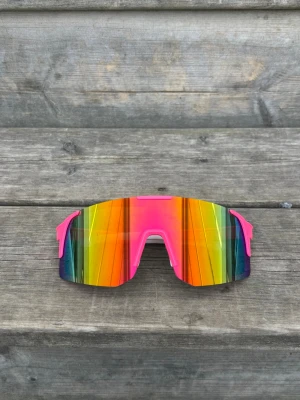 Rosa Färgglada sportiga solglasögon - Skickar gärna i bundle. Säljer ett par riktigt coola solglasögon med spegelglas i regnbågsfärger och rosa bågar. De har en sportig, futuristisk design med breda linser som täcker bra. Perfekta för dig som vill sticka ut och gillar färg!
