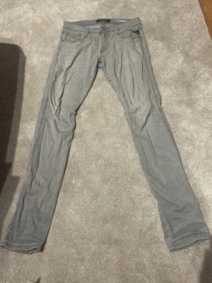 Gråa anbass jeans från Replay - Säljer ett par gråa slim fit jeans från Replay med klassisk femficksdesign och snygga detaljer. Jeansen har en modern passform och är tillverkade i mjukt denim-material som ger en skön känsla. Perfekta för dig som gillar stilrena och trendiga jeans.