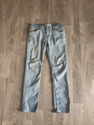 Ljusblå raka jeans från Levi's - Ljusblå jeans från Levi's med klassisk femficksdesign och raka ben. Jeansen har en snygg tvättad look och detaljer i kopparfärgad metall. Perfekta för en avslappnad stil och passar till det mesta i garderoben. De är lite stora i storleken