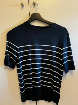 Svart och vit randig topp från 157 - Svart topp med vita horisontella ränder från 157. Modellen har rund halsringning och korta ärmar. Perfekt för en stilren och avslappnad look. Materialet känns mjukt och lätt, vilket gör den skön att bära hela dagen.