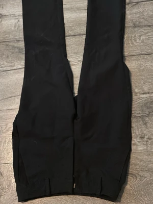 Svarta kostymbyxor med raka ben - Snygga svarta kostymbyxor med raka ben och diskreta bakfickor. Byxorna har hällor för skärp och en klassisk, stilren look. Perfekta för dig som vill ha en clean och enkel stil. Materialet känns mjukt och följsamt.