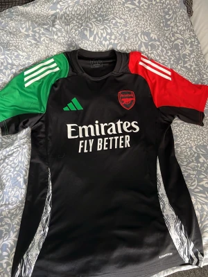 Arsenal Adidas svart träningströja - Säljer denna svarta arsenal träningströja med gröna/röda detaljer. Från adidas, storlek M. (OBS, används 2 gånger men aldrig under träning, endast som vardaglig T-shirt). Perfekt för vardaglig användning eller till träning!