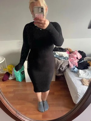 Svart ribbad klänning med öppen rygg - Svart, ribbad klänning med lång ärm och snygg öppen ryggdetalj. Klänningen är kroppsnära och går till knäna, perfekt för dig som gillar en stilren och trendig look. Materialet är stretchigt och bekvämt.
