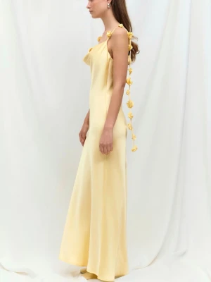 Ljusgul långklänning med blomdetaljer - Elegant ljusgul långklänning med smala axelband dekorerade med blommor som hänger ner längs ryggen. Klänningen har öppen rygg och är tillverkad i ett mjukt, glansigt material som ger ett lyxigt intryck. Perfekt för dig som vill sticka ut med en unik och feminin look. Lappen sitter kvar.