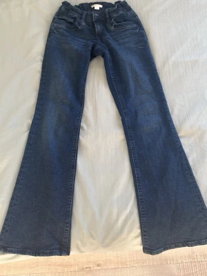 Mörkblå bootcut jeans med resårmidja - Snygga mörkblå bootcut jeans med resår i midjan och klassiska fem fickor. Jeansen har utsvängda ben och är tillverkade i mjukt denimtyg som ger en bekväm passform. Perfekta för dig som gillar en retroinspirerad look.