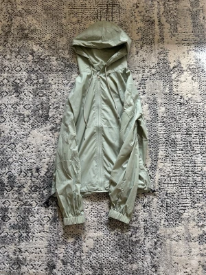 Risky Universe Windbreaker M - Snygg ljusgrön vindjacka med huva och dragkedja framtill. Jackan har resår vid ärmsluten och en diskret logga på ärmen. Perfekt för blåsiga dagar och enkel att packa ner i väskan.
