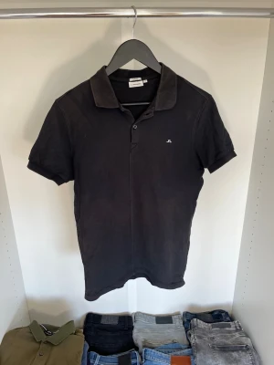 Svart pikétröja från J.Lindeberg - Svart pikétröja från J.Lindeberg med klassisk krage och liten logga på bröstet. Slim fit-modell med korta ärmar och knappslå framtill. Hör gärna av dig vid frågor!