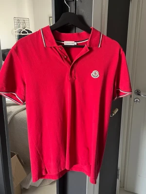 Röd pikétröja från Moncler - Röd moncler piké som är köpt på garmsmarket. Använder inte längre. Perfekt inför sommaren. Storlek L sitter som M