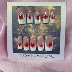 Famous (S); Medium Square - Snygga handgjorda press-on naglar i en nude och handmålad vit fransk design med röda stjärnor. Naglarna har en rak, medium lång form och är handgjorda Perfekt för dig som vill ha en unik och trendig look.S: 15 mm, 11,5 mm, 12 mm, 11 mm, 9 mm 