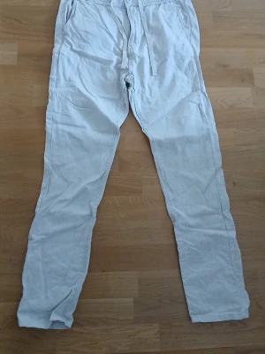 Beige linnebyxor - Snygga Beiga linnebyxor frän kappahl med avslappnad passform och dragsko i midjan. Byxorna har sidfickor och en bakficka med knapp. Perfekta för en chill och stilren look. Materialet är svalt och luftigt linne. Dragkedja, knapp och snöre. Struks innan plagget skickas. Storlek S. Oanvända.