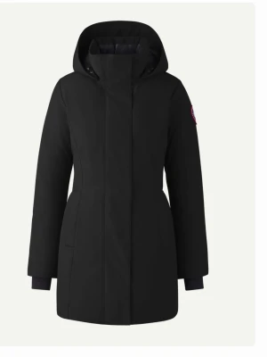 Svart parkas från Canada Goose - Stilren svart parkas med huva från Canada Goose. Jackan har en rak passform, diskret logotyp på ärmen och dolda fickor i sidorna. Perfekt för kalla dagar med sin långa modell och ribbade muddar vid ärmslut.
