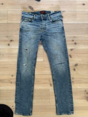Blå slitna jeans från Jack & Jones - Snygga blå jeans från Jack & Jones med slitningar och distressed detaljer på benen. Klassisk femficksmodell med dragkedja och knapp. Jeansen har en smal passform och är tillverkade i denim med lätt stretch för extra komfort.