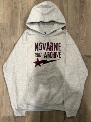 Novarné 1987 Archive Star Hoodie Size M Grå - Stilren hoodie med en avslappnad passform och tydlig archive-känsla, designad för att sitta något löst och ge en modern silhuett. Passar perfekt för en clean och minimalistisk stil, både som den är eller i lager-på-lager outfits.  Mått: bröstvidd 53 cm, axelbredd 56,5 cm, längd 68,5 cm, ärmlängd 58 cm, midja 43 cm.  Skick: nyskick, endast testad.