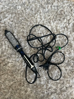 Värmeborste  - Elektrisk rundborste från Hot Tools med svart och silverfärgad design. Handtaget är svart med blå detaljer och borstdelen har vita och svarta piggar. Perfekt för att styla och skapa volym i håret. Utrustad med sladd och EU-kontakt.