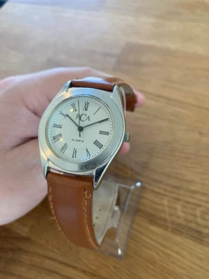 Vintage PCA Quartz Armabandsur - Ett klassiskt äldre armbandsur från PCA med Quartz batteri och ett brunt läderarmband. Urtavlan är vit med romerska siffror. Boetten är i silverfärgad metall. Trasigt armband, skick enligt bilder. Behöver bara nytt batteri.  Mitt pris: 189 SEK  Skickas snabbt och spårbart. Skriv vid frågor och se gärna mina andra annonser!
