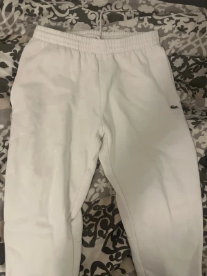 Vita slim fit mjukisbyxor Lacoste - Snygga vita mjukisbyxor från Lacoste i slim fit-modell. Byxorna har resår i midjan med dragsko och den klassiska Lacoste-loggan broderad på benet. Perfekta för en chill och stilren look.