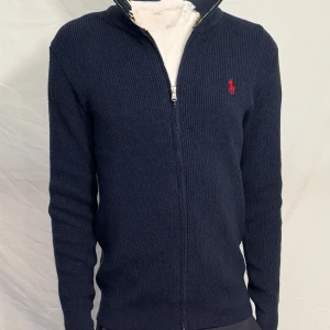 Ralph Lauren tröja - Stilren mörkblå zip-kofta från Ralph Lauren i fint skick. Ribbstickad design med dragkedja och klassisk broderad logga på bröstet. Pris går att diskuteras