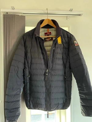 Mörkblå dunjacka från Parajumpers - Snygg mörkblå dunjacka från Parajumpers med klassisk quiltad design och gul detalj vid kragen. Jackan har hög krage, dragkedja framtill och logotyp på ärmen. #parajumper #jacka
