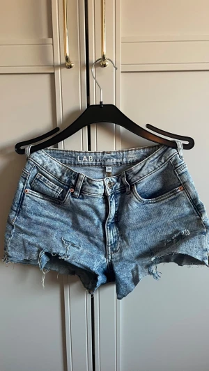 Blå denimshorts från Gekås Ullared! - Snygga blå denimshorts från Gekås Ullared med råa kanter och slitna detaljer. Klassisk femficksmodell med knapp- och dragkedjestängning. Perfekta för varma dagar och en avslappnad stil.