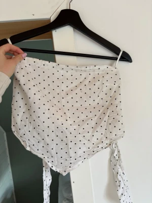 Vit prickig axelbandslös tubtopp - Jättefin prickig axelbandslös topp! Söt nu till sommaren. Den har lite missfärgningar åt det gula hållet men det är inget som märks av. Går även att knyta i ryggen