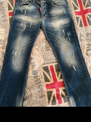 Dsquared2 blå slitna jeans herr - Säljer ett par blå jeans från Dsquared2 med cool slitning och distressed detaljer. Jeansen har klassisk femficksmodell, röd söm på insidan och är tillverkade i denim. Perfekta för dig som gillar streetwear och vill sticka ut lite extra.