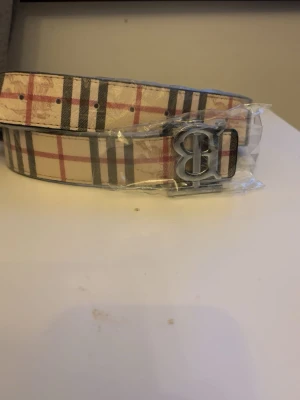 Beige designer bälte  - Beige designer bälte. Mönster med olika färger och en silver buckla helt ny och oanvänd. 