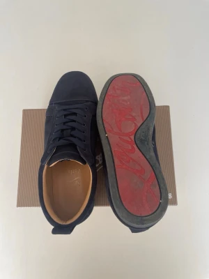 Mörkblå sneakers från Louboutin - Snygga mörkblå sneakers från Christian Louboutin i mocka med klassisk röd sula och diskret logga på sidan. Fick dessa i födelsedags present för snart ett år sedan men har inte använt dom på ett bra tag då jag känner att det inte riktigt är min stil längre. Låda och allting på bilden ingår självklart också i köpet. Dustbagsen kom inte med på bilden då dom låg i skolådan. Kom PM för mer info 🫶(Storlek 45) (Skick 7/10) Man ser att dom är använda men jag fräschar upp dom innan frakt! 👊💪