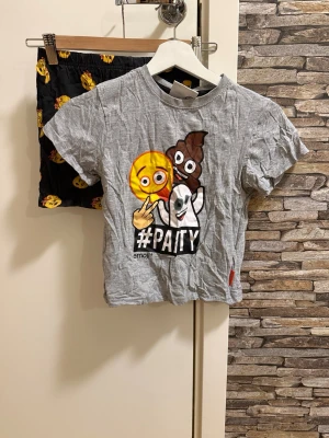 Emoji pyjamas  - Rolig pyjamas med grå t-shirt med stora emoji-figurer och texten #PARTY på framsidan. Tillhörande svarta shorts med gula emoji-mönster. Perfekt för chillkvällar hemma. Mjukt och bekvämt material, troligen bomull.