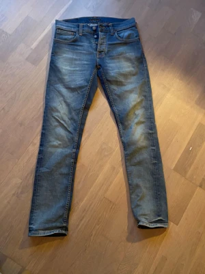 Blå slim fit jeans från Nudie Jeans - Snygga blå slim fit jeans från Nudie Jeans med klassisk femficksdesign och knappgylf. Jeansen har en lätt tvättad look och smala ben. Perfekta för dig som gillar en modern och stilren stil. Storlek W30 L32