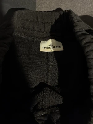 Svarta shorts från Stone Island - Svarta shorts från Stone Island med elastisk midja och en ficka på sidan med den klassiska logotypen. Tillverkade i mjuk bomull för skön känsla och avslappnad passform. Perfekta för chill dagar eller när du vill ha en clean streetwear-look.