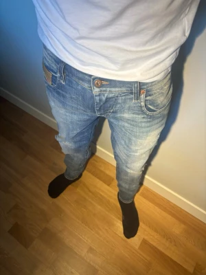  jeans med slitningar från Diesel - Säljer ett par ljusblå slim fit jeans ifrån Diesel med snygga slitningar och tvättade detaljer. Jeansen har klassisk femficksdesign, knappgylf och smal passform. Perfekta för en avslappnad och trendig look. Extremt unika och snygga! 