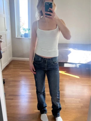 Blå raka jeans med normal passform - Säljer ett par vintage blå jeans med rak passform och normal midja. Jeansen har fem fickor och subtila sömdetaljer på bakfickorna. Perfekta till vardags och lätta att matcha med olika stilar.