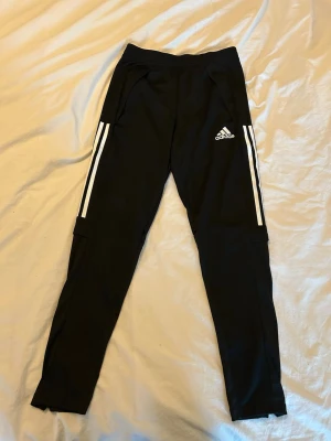 Svarta Adidas mjukisbyxor med vita ränder - Svarta mjukisbyxor från Adidas med klassiska vita ränder längs sidorna. Passar bra på mig som är 176 cm!💗