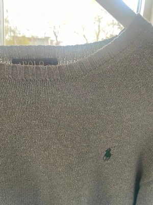 Grå stickad tröja från Polo Ralph Lauren - Snygg grå stickad tröja från Polo Ralph Lauren med rund halsringning och klassisk grön broderad logga på bröstet. Tröjan har ribbade muddar vid ärmslut och nederkant. Perfekt för lager-på-lager och enkel att matcha. Säljer pga den inte passar längre. Passar jättebra tillsammans med skjortor och liknande, samtidigt som den är sjukt stilren! När det kommer till storleken står det M men skulle säga att den är mer S i storlek om du är ca 170 eller under passar den dig! Inga defekter eller skador! 