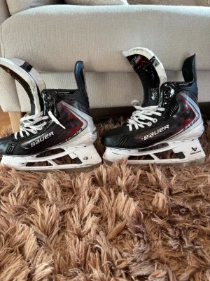 Bauer Vapor hockeyskridskor svart/vit - Säljer ett par Bauer Vapor Fly40 hockeyskridskor i svart, vitt och röda detaljer. De är knappt använda utan har enbart använts på träning. Nypris:5500